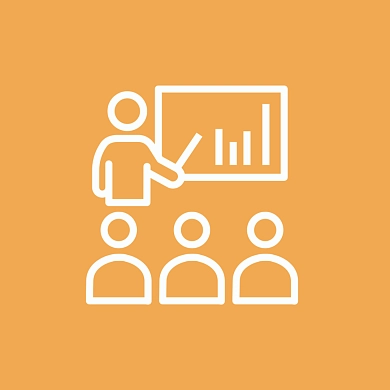 Menschen, die vor einer Tafel sitzen und eine lehrende Person anschauen